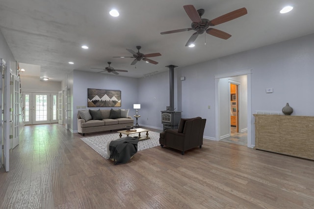 living room featuring french doors, wood-type flooring, ceiling fan, and a wood stove