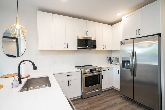 kitchen featuring dark hardwood / wood-style floors, tasteful backsplash, white cabinetry, appliances with stainless steel finishes, and pendant lighting