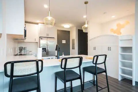 kitchen featuring dark hardwood / wood-style floors, stainless steel fridge, pendant lighting, white cabinets, and a kitchen bar