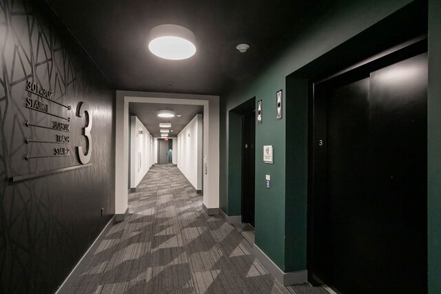 hallway with dark carpet and elevator