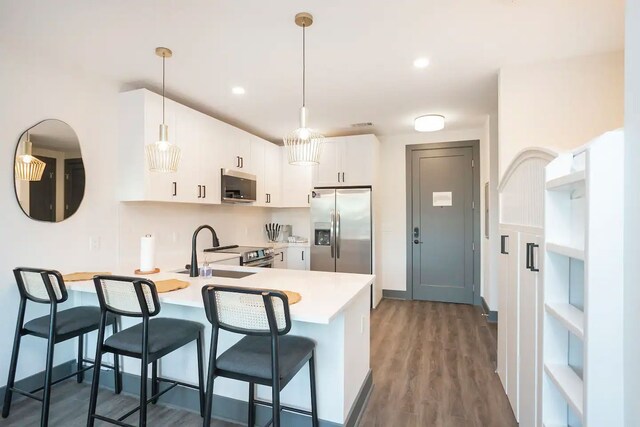 kitchen with stainless steel appliances, hardwood / wood-style flooring, white cabinetry, sink, and pendant lighting