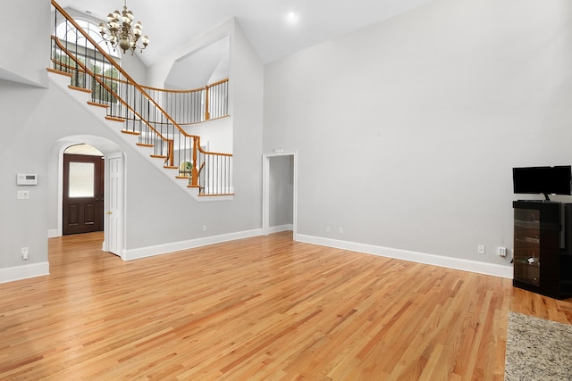 unfurnished living room featuring a chandelier, light wood-type flooring, and high vaulted ceiling