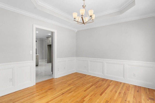 spare room with a tray ceiling, crown molding, a chandelier, and hardwood / wood-style flooring