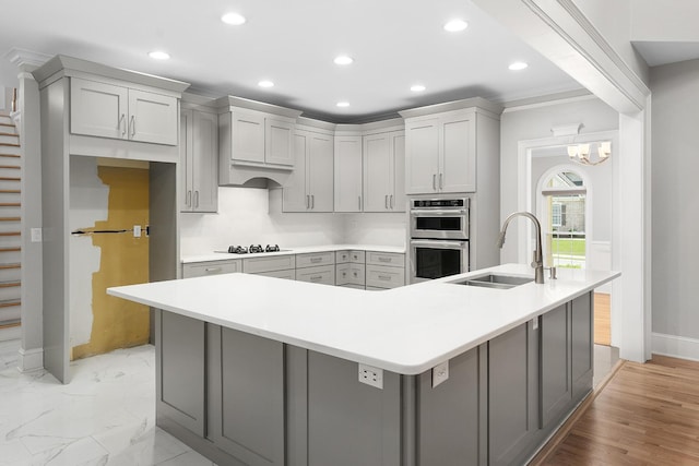 kitchen with gray cabinetry, sink, double oven, black cooktop, and a spacious island