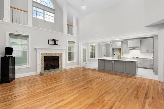 unfurnished living room featuring a high end fireplace, light hardwood / wood-style flooring, high vaulted ceiling, and sink