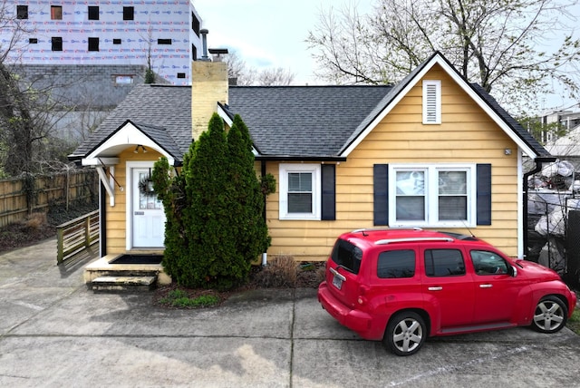 bungalow featuring roof with shingles, a chimney, and fence