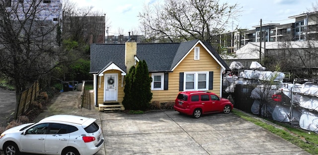 bungalow-style home featuring entry steps, roof with shingles, fence, and a chimney