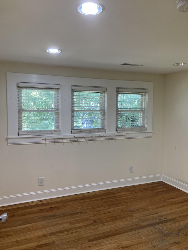 spare room featuring dark wood-type flooring, recessed lighting, a healthy amount of sunlight, and baseboards