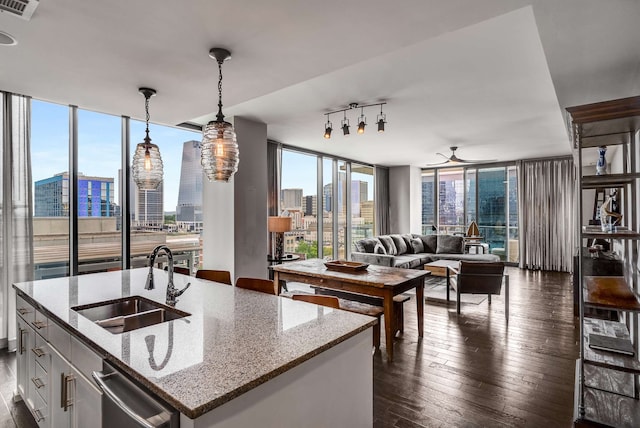 kitchen with a center island with sink, sink, hanging light fixtures, dark hardwood / wood-style floors, and light stone counters