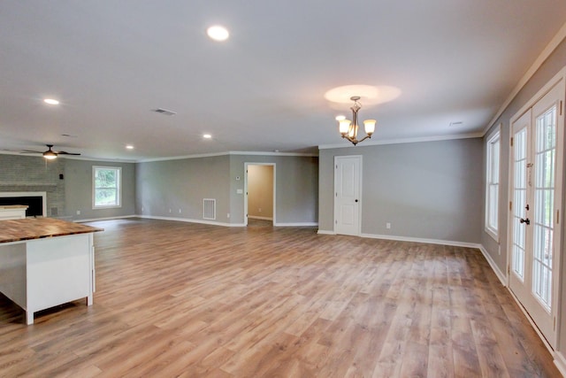 unfurnished living room with crown molding, a fireplace, light hardwood / wood-style floors, and ceiling fan with notable chandelier