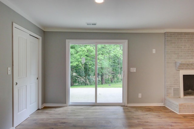 unfurnished living room featuring ornamental molding, light hardwood / wood-style flooring, and a brick fireplace