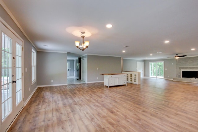 unfurnished living room featuring french doors, ceiling fan with notable chandelier, crown molding, light wood-type flooring, and a fireplace