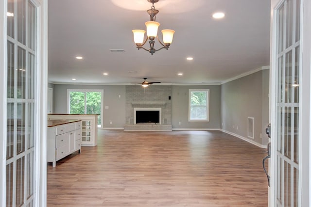 unfurnished living room with crown molding, light hardwood / wood-style flooring, ceiling fan with notable chandelier, and a brick fireplace