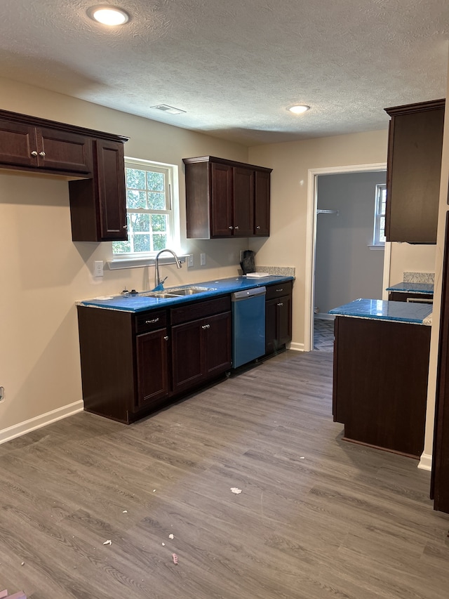 kitchen with wood-type flooring, a textured ceiling, stainless steel dishwasher, and sink