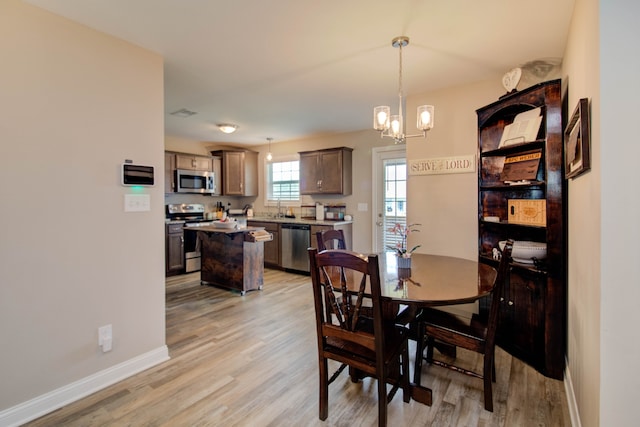 dining space featuring light wood-type flooring, sink, and an inviting chandelier