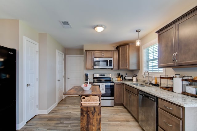 kitchen with hanging light fixtures, sink, appliances with stainless steel finishes, and light hardwood / wood-style flooring