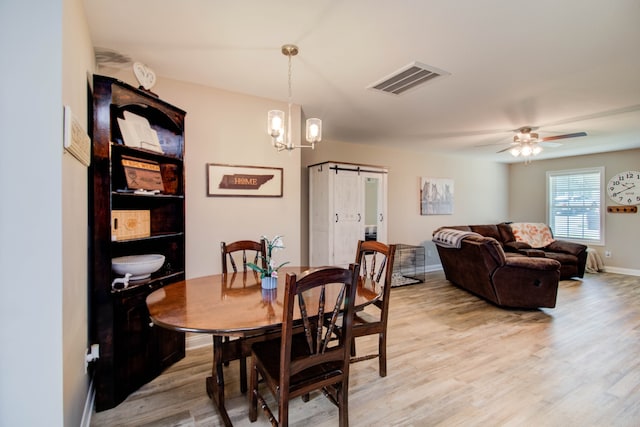 dining room featuring ceiling fan with notable chandelier, a barn door, and light wood-type flooring