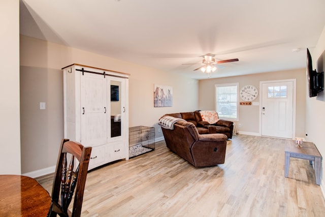 living room featuring a barn door, light hardwood / wood-style floors, and ceiling fan