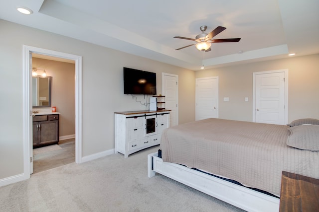 bedroom featuring a raised ceiling, ensuite bath, ceiling fan, and light colored carpet