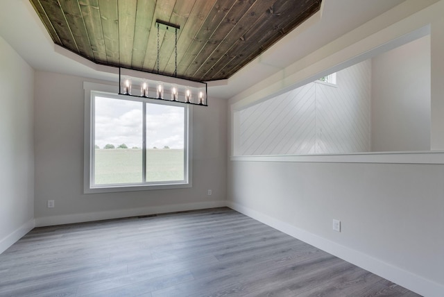 unfurnished dining area featuring light wood-type flooring, a tray ceiling, and wooden ceiling