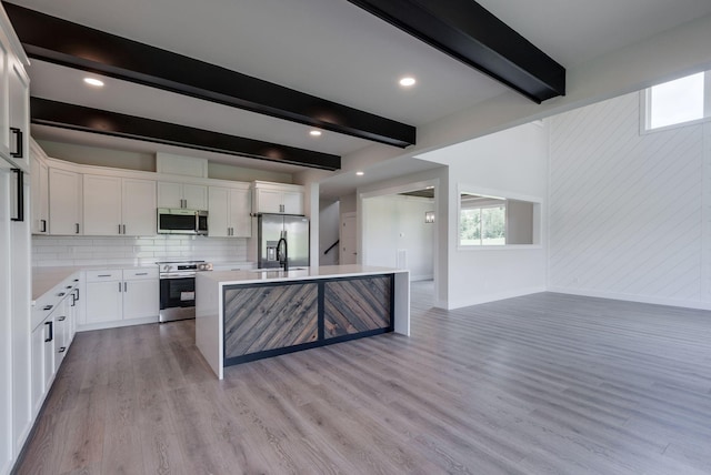 kitchen featuring appliances with stainless steel finishes, beam ceiling, light hardwood / wood-style flooring, white cabinets, and a kitchen island