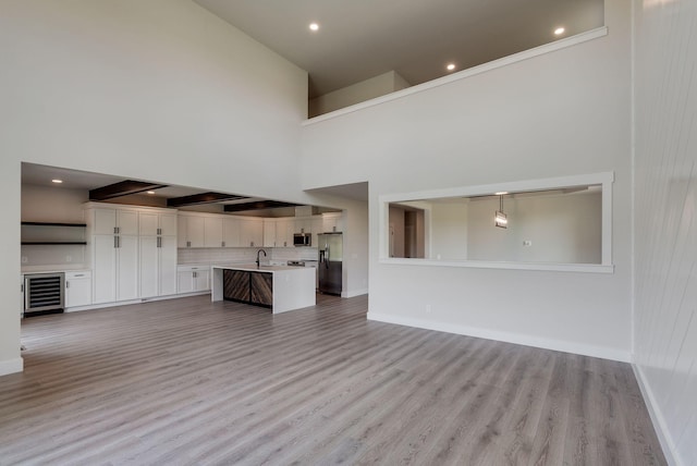 unfurnished living room with a towering ceiling, beverage cooler, and light wood-type flooring