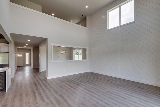 unfurnished living room with a towering ceiling, light wood-type flooring, and plenty of natural light