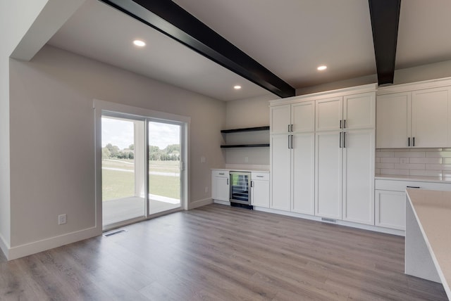 kitchen with beam ceiling, white cabinetry, beverage cooler, tasteful backsplash, and light wood-type flooring