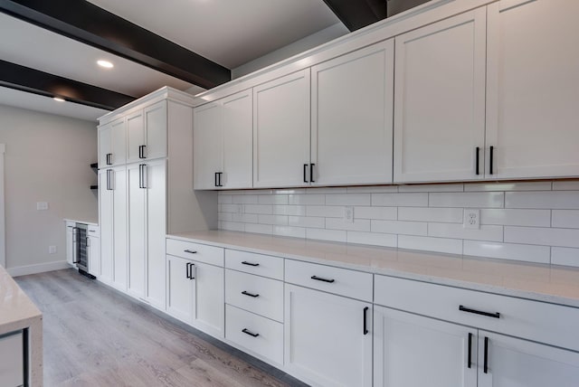 kitchen featuring white cabinets, light hardwood / wood-style flooring, decorative backsplash, beamed ceiling, and light stone counters