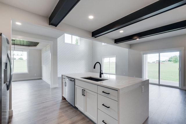 kitchen with stainless steel appliances, a kitchen island with sink, sink, beamed ceiling, and white cabinets