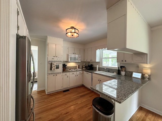 kitchen featuring kitchen peninsula, appliances with stainless steel finishes, sink, light hardwood / wood-style floors, and white cabinetry