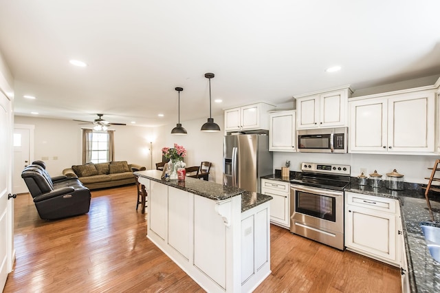 kitchen with stainless steel appliances, white cabinetry, open floor plan, a kitchen bar, and decorative light fixtures