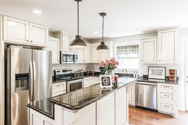 kitchen with appliances with stainless steel finishes, dark stone counters, a kitchen island, and hanging light fixtures