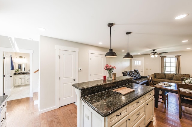 kitchen featuring dark stone counters, a kitchen island, open floor plan, decorative light fixtures, and light wood-type flooring