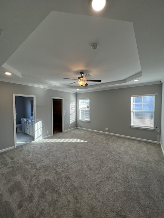 unfurnished bedroom featuring crown molding, ensuite bathroom, a raised ceiling, and carpet