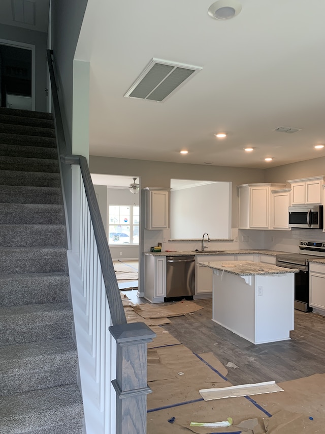 kitchen featuring sink, stainless steel appliances, light stone countertops, white cabinets, and a kitchen island