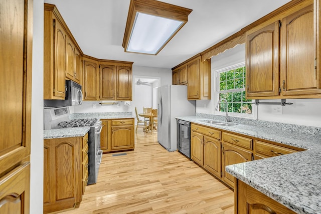 kitchen with light stone counters, ceiling fan, sink, black appliances, and light hardwood / wood-style flooring