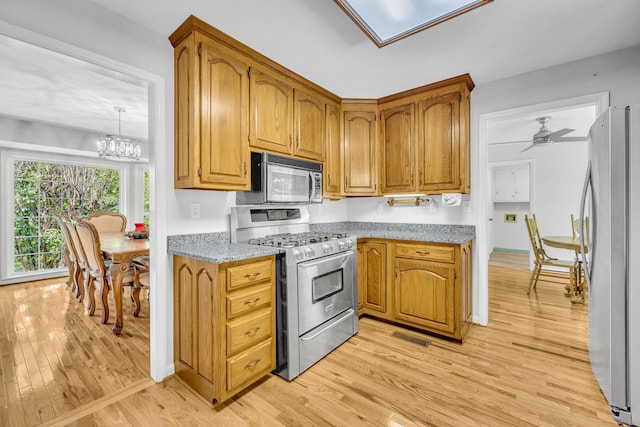 kitchen featuring ceiling fan with notable chandelier, stainless steel appliances, light hardwood / wood-style flooring, and light stone counters