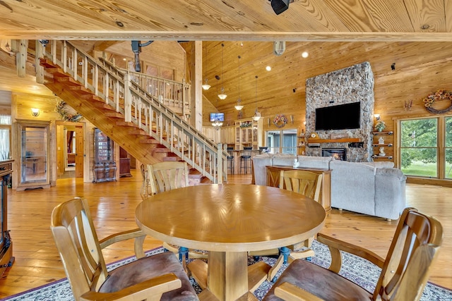 dining space featuring light hardwood / wood-style flooring, wood walls, high vaulted ceiling, wooden ceiling, and a stone fireplace