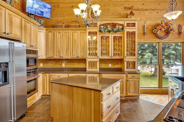 kitchen with light brown cabinets, dark stone countertops, a kitchen island, pendant lighting, and appliances with stainless steel finishes