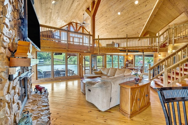 living room featuring wood ceiling, a stone fireplace, light wood-type flooring, ceiling fan, and high vaulted ceiling