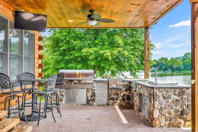 view of patio featuring an outdoor kitchen, ceiling fan, exterior bar, and a water view