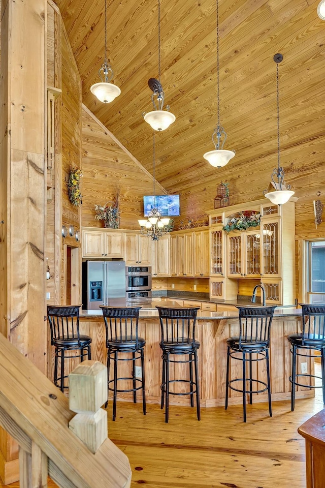 kitchen with a kitchen breakfast bar, appliances with stainless steel finishes, high vaulted ceiling, light brown cabinets, and decorative light fixtures