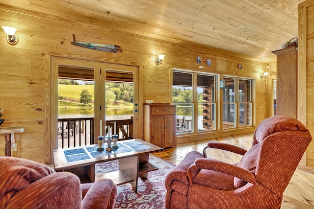 living room featuring light hardwood / wood-style floors, wood ceiling, a water view, and wooden walls