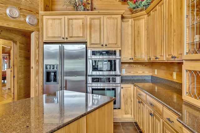 kitchen featuring stainless steel appliances, light brown cabinets, dark tile patterned flooring, wood walls, and dark stone counters