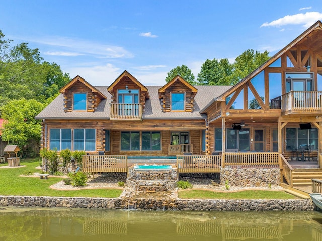 back of property with a balcony, a jacuzzi, and a water view