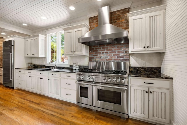 kitchen featuring white cabinetry, sink, high end appliances, light wood-type flooring, and wall chimney exhaust hood