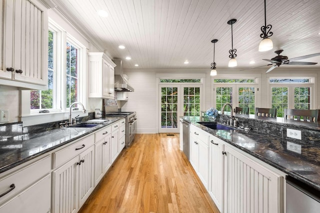 kitchen featuring sink, white cabinetry, hanging light fixtures, stainless steel appliances, and wall chimney exhaust hood