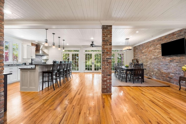 interior space featuring decorative columns, brick wall, a wealth of natural light, and light hardwood / wood-style flooring