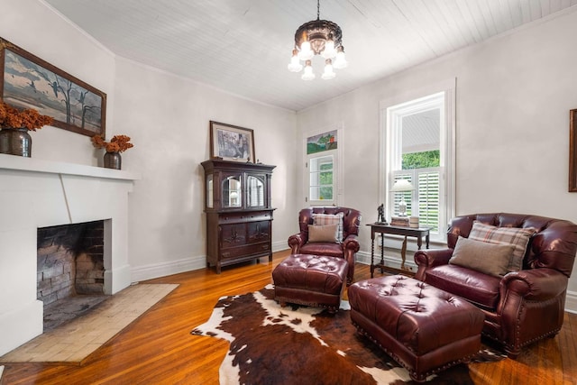 living area featuring a tiled fireplace, a notable chandelier, crown molding, and wood-type flooring